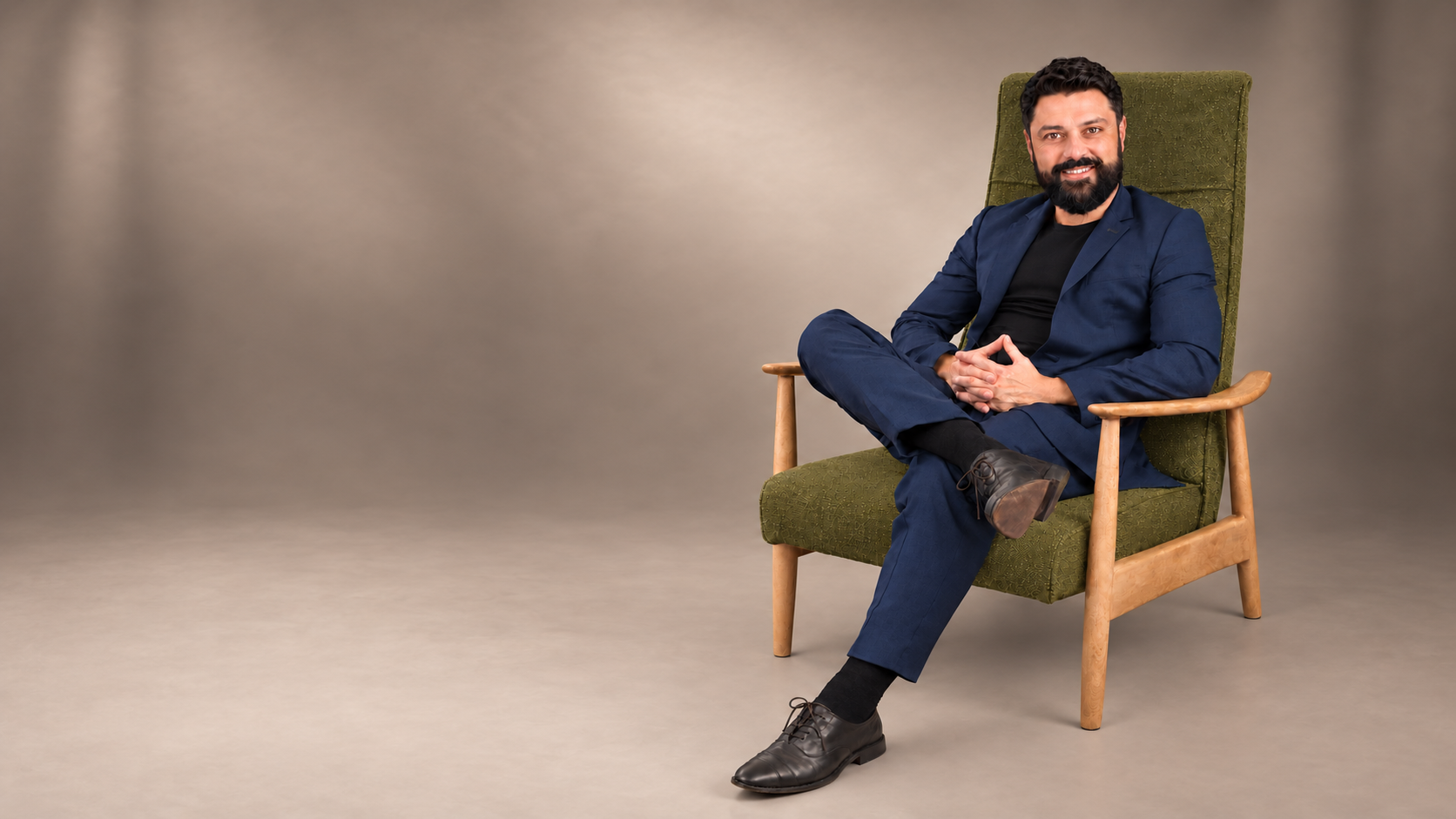 Oscar Caballero seated in his olive mid-century chair